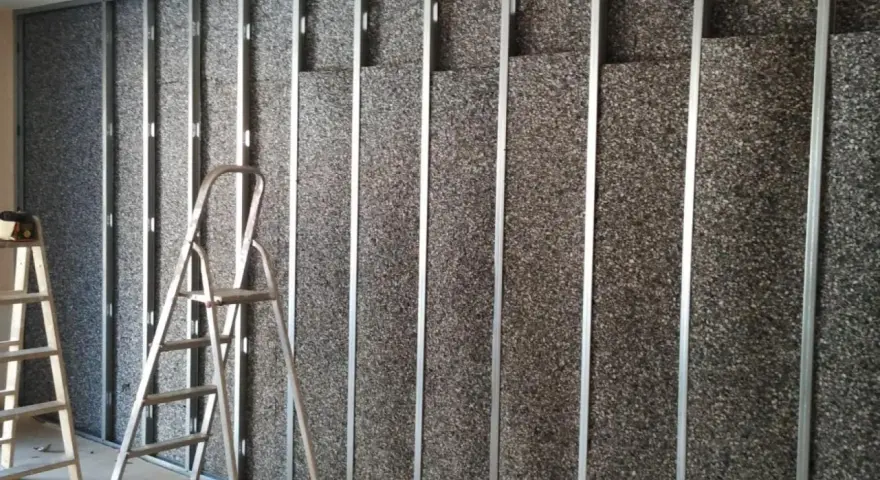 Instalación de material para insonorizar pared. Escaleras apoyadas contra la estructura metálica y el panel aislante.