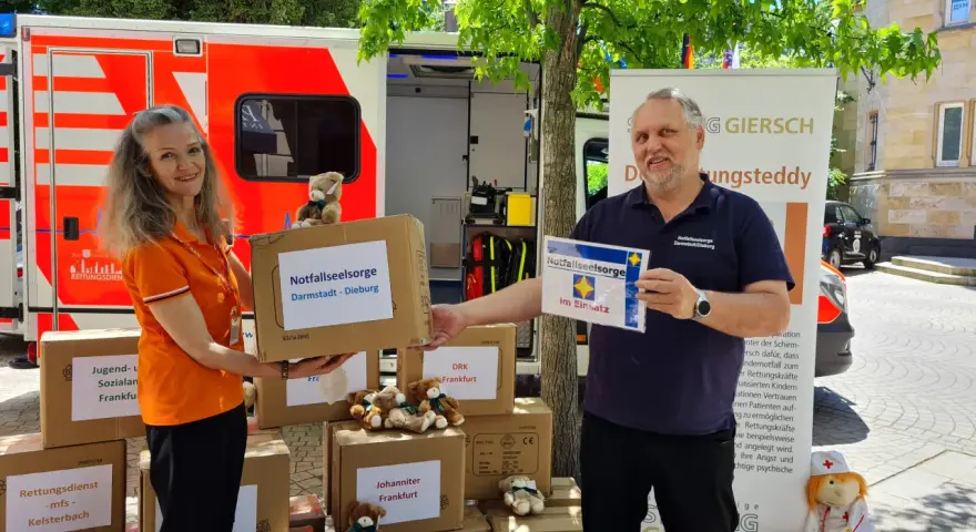 Zwei Personen vor einem Rettungswagen präsentieren Kartons für die Notfallseelsorge. Sie sind bereit, als Notfallseelsorger zu helfen.
