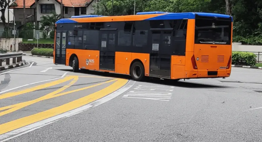 Pomarańczowo-niebieski autobus miejski na zakręcie drogi z żółtymi pasami.