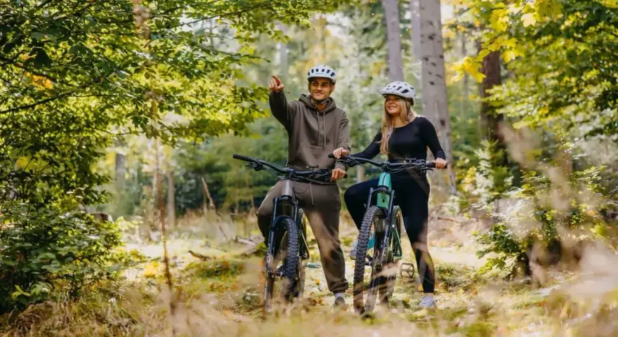 Para rowerzystów w kaskach na leśnej ścieżce. Mężczyzna wskazuje drogę, odkrywając piękną trasę w Szklarskiej Porębie.