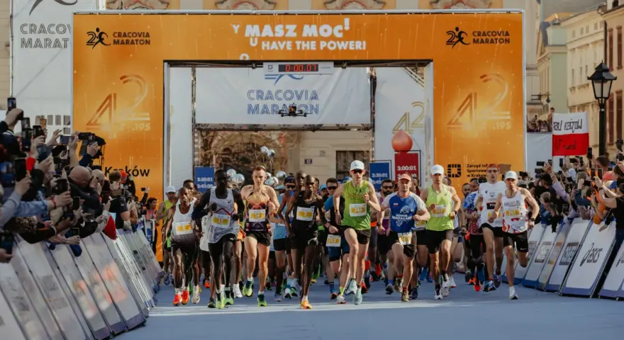 Zawodnicy przekraczają linię startu Maratonu Cracovia. Tłum kibiców z telefonami dokumentuje to wydarzenie.