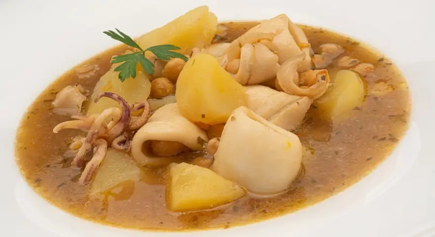 Guiso de garbanzos con trozos de calamar, patatas y perejil en un plato blanco.