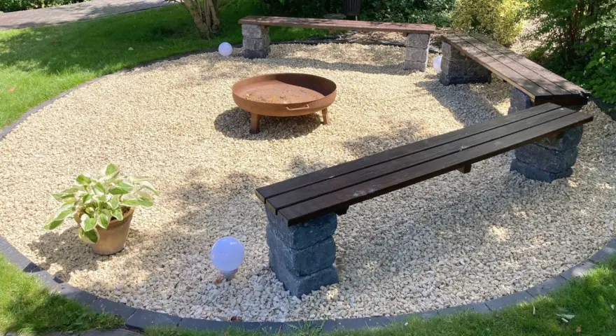 Gemütliche Sitzecke im Garten mit Kiesboden, Feuerstelle und Holzbänken. Perfekt für laue Sommerabende.