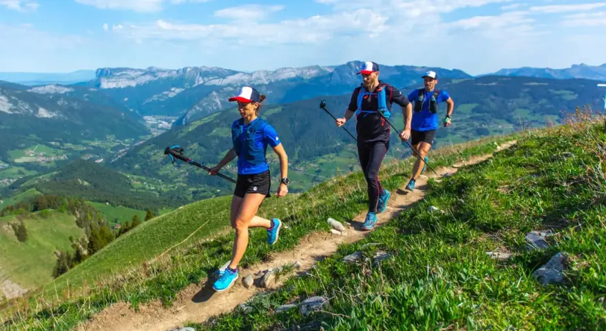 Trzy osoby uprawiające speed hiking na górskim szlaku, ciesząc się pięknymi widokami.