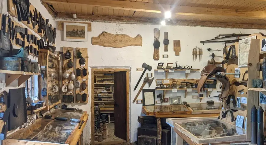 Wnętrze muzeum historii Bieszczad. Eksponaty to narzędzia, broń, siodła i przedmioty codziennego użytku.
