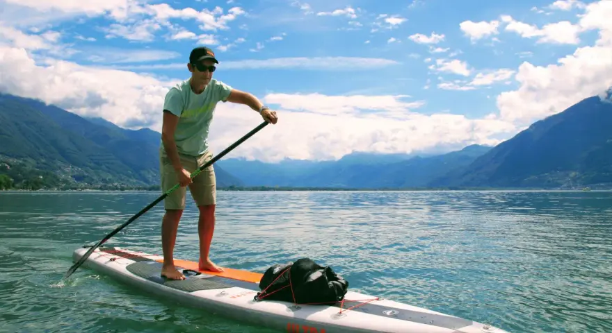 Mann auf SUP-Board mit Paddel, genießt die Geschwindigkeit auf dem See vor einer Bergkulisse.