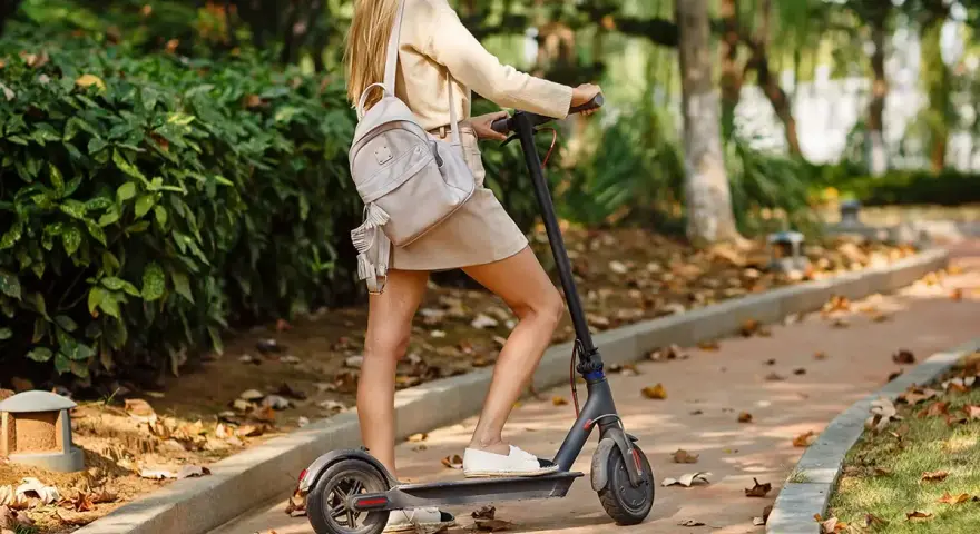 Ragazza su monopattino elettrico in un parco autunnale. Ricorda l'obbligo casco monopattino per la tua sicurezza.