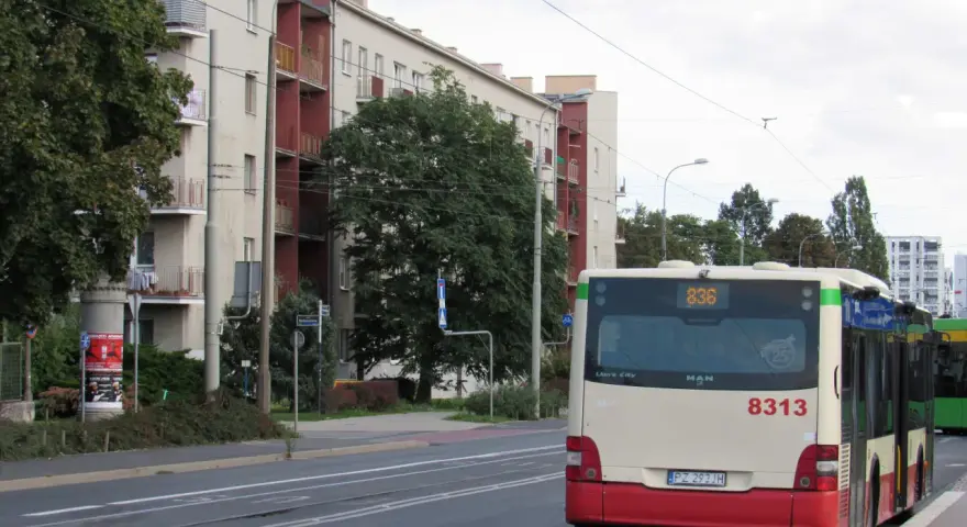 Autobus 8313 z numerem linii 836 czeka na przystanku. W tle budynki mieszkalne i drzewa.