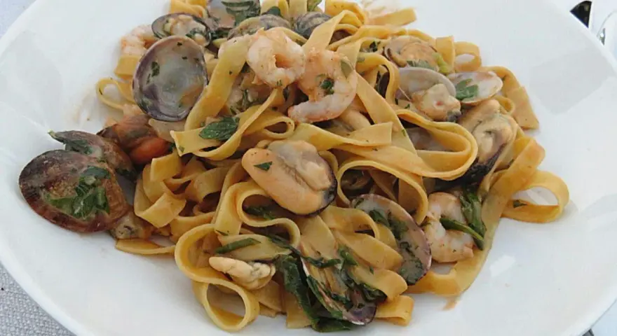 Un piatto invitante di tagliatella di mare con gamberi, cozze e vongole, condita con erbe fresche.