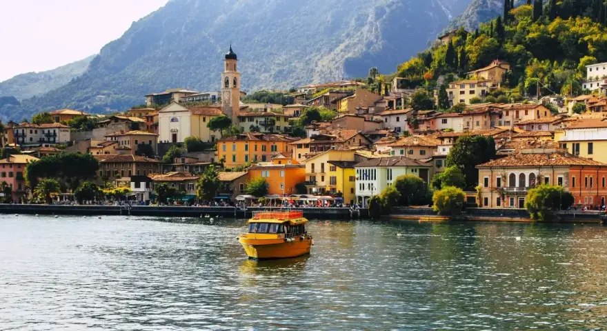 Un giallo battello solca il lago, dirigendosi verso il pittoresco borgo di Limone sul Garda, con le sue case colorate aggrappate alla montagna.