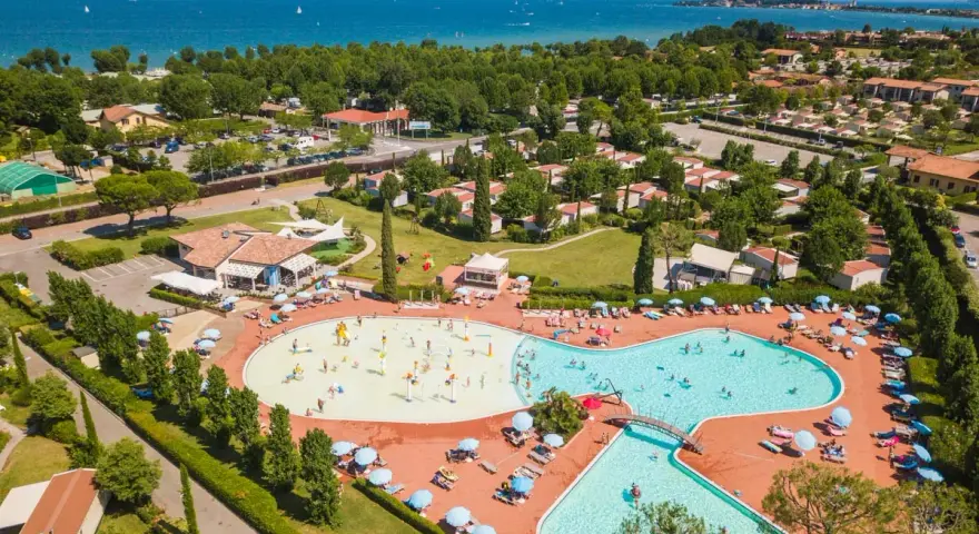 Widok z lotu ptaka na kompleks basenów i domków kempingowych w Sirmione. Woda lśni w słońcu, a ludzie cieszą się wakacjami na łonie natury.