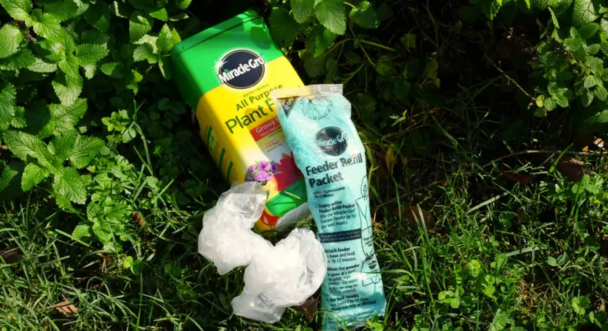 Miracle-Gro plant food and feeder refill packet lie on grass. While not inherently toxic, proper use is key to avoid harming plants.
