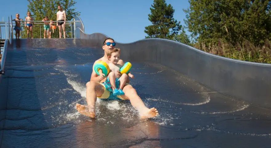 Vater und Sohn rutschen lachend die Wasserrutsche im Bostalsee Strandbad hinunter.