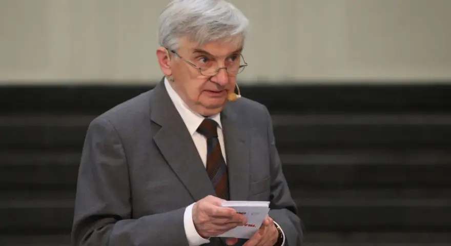 Starszy mężczyzna w garniturze, który prowadzi jeden z dziesięciu, trzyma kartkę.