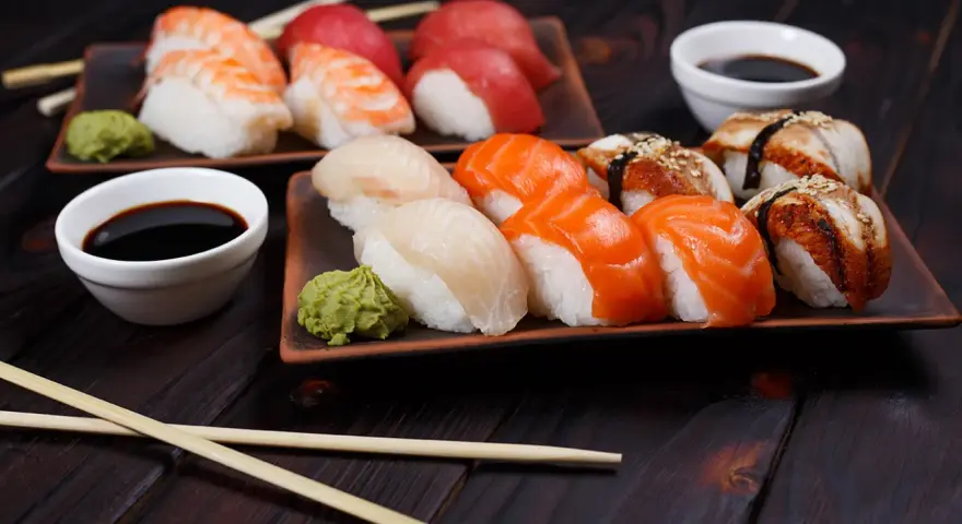 Różnorodne rodzaje sushi: nigiri z krewetką, łososiem, białym rybą i węgorzem, podane z wasabi i sosem sojowym.