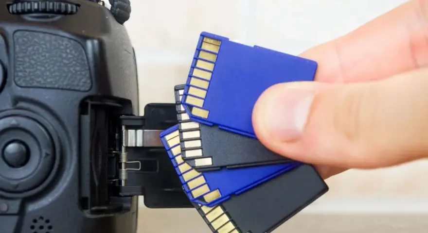 Main tenant, une main s'apprête à insérer une carte SD dans un appareil photo. Il est temps de choisir la carte SD parfaite pour vos souvenirs.