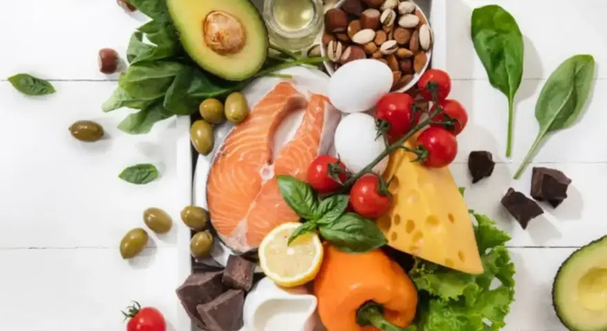 Składniki na dieta keto jadłospis: łosoś, awokado, jajka, ser, orzechy, oliwki, warzywa i gorzka czekolada.
