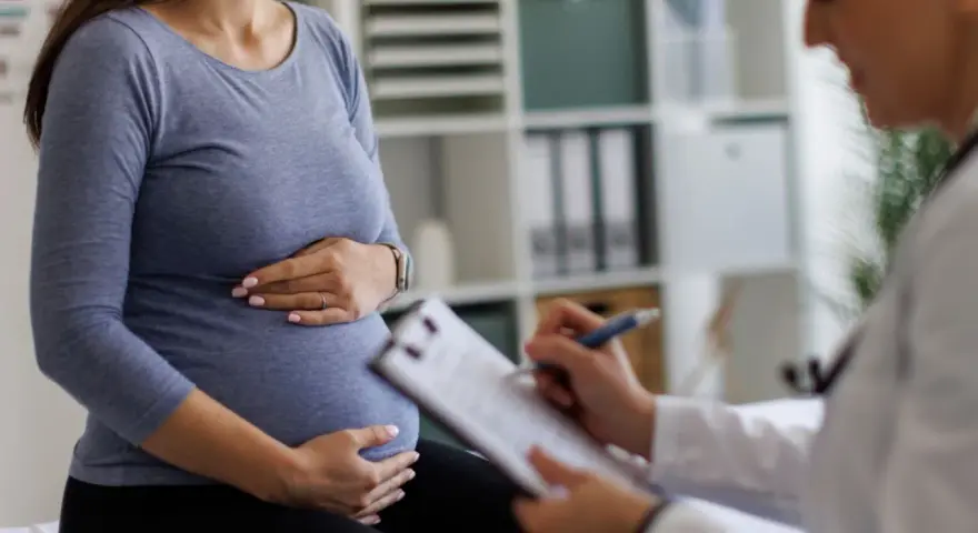Visita medica: una donna incinta tiene la pancia mentre il medico annota sul foglio, forse il tracciato delle contrazioni preparatorie.