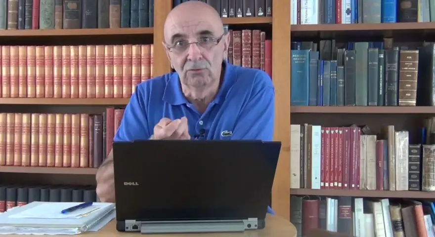 Un homme parle devant un ordinateur portable, entouré de rayonnages remplis de livres anciens, rappelant les archives départementales 85.