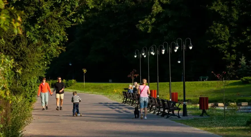 Rodzina spaceruje po parku z dzieckiem na hulajnodze i psem.