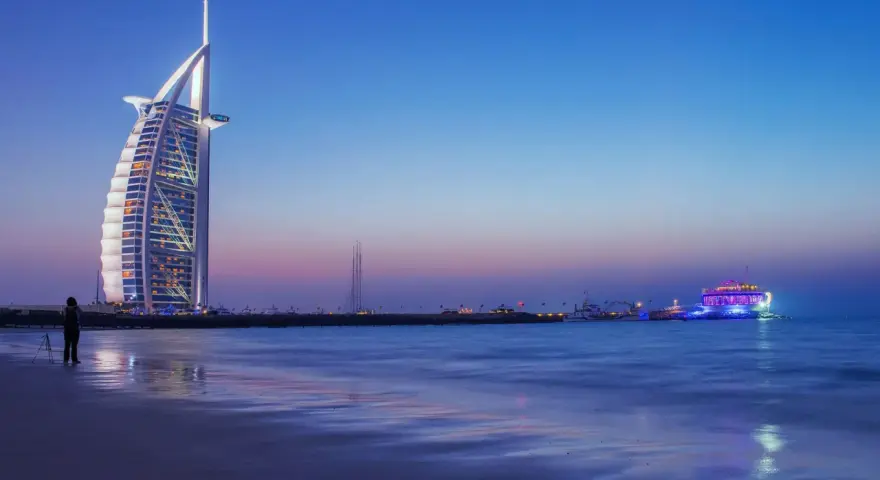 Zachód słońca nad Zatoką Perską. Widok na hotel Burj Al Arab i oświetloną łódź. Ceny w Dubaju mogą być wysokie, ale widoki są bezcenne.