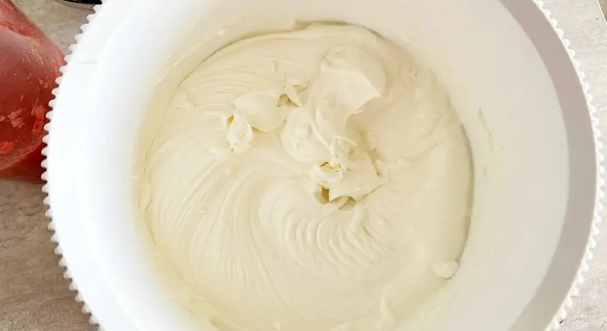 Gładki, puszysty **prosty krem z mascarpone bez śmietany** w białej misie, gotowy do deseru. Obok miski widać miseczkę z truskawkami.