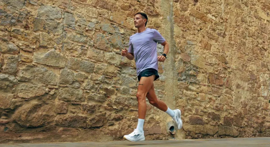 Uomo con tatuaggio corre lungo un muro di pietra. La sua tecnica di pronatore corsa è fluida e potente.