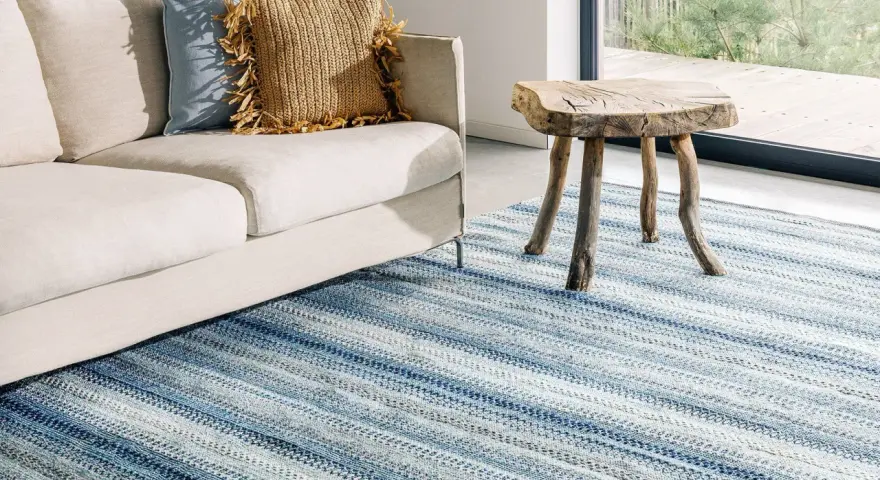En ljus soffa med kuddar och en rustik pall står på en randig blå matta. Perfekt inspiration matta vardagsrum för en avslappnad stil.