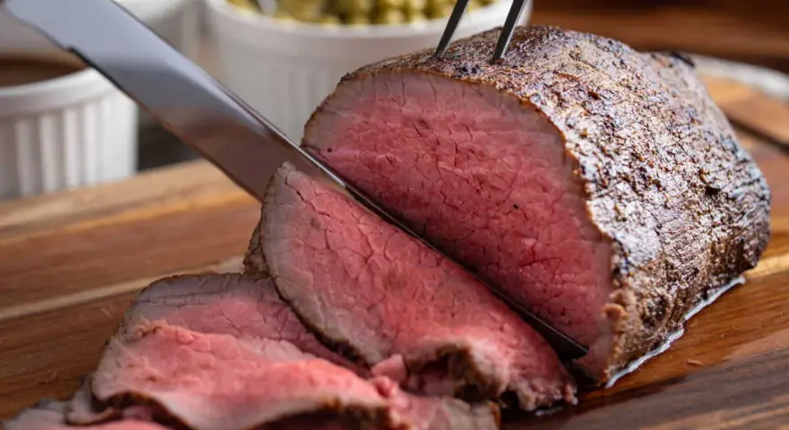 Un délicieux roti de boeuf, coupé en fines tranches rosées, est prêt à être servi avec des accompagnements.