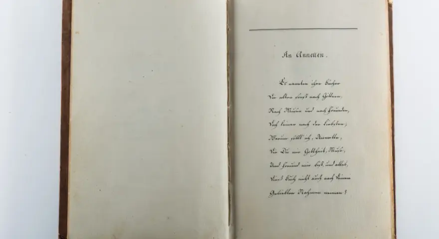 Ein aufgeschlagenes Buch mit handschriftlichem Gedicht auf der rechten Seite.