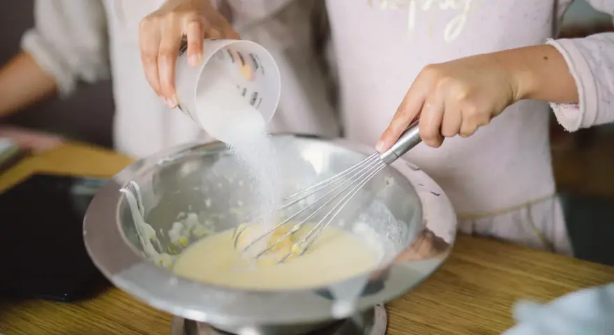 Préparation de la pâte à crêpes : on ajoute du sucre dans le bol avec un fouet. C'est la base de la recette des crêpes.