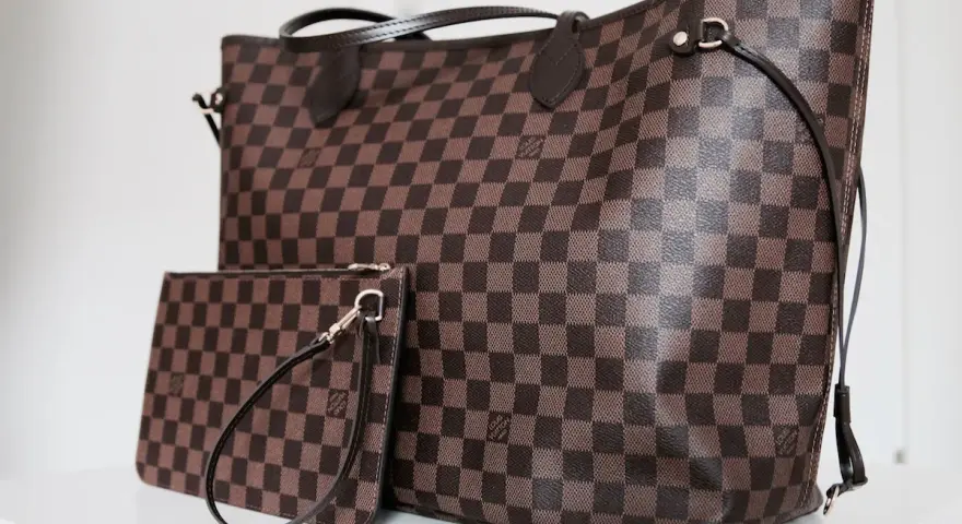 Duża torebka Louis Vuitton w kratkę, obok mniejsza kosmetyczka. Klasyczny wzór Damier Ebene.