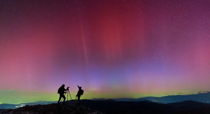 Due fotografi ammirano l'incredibile aurora boreale in Italia, con sfumature rosa e viola che danzano nel cielo stellato.