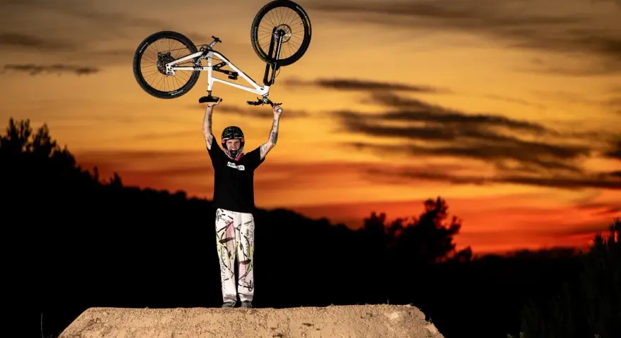 Tomas Lemoine triumphantly raises his bike against a fiery sunset, a champion on the dirt jump.