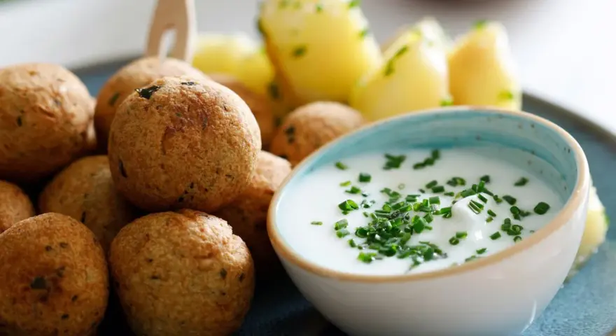 Polpette di ceci dorate e croccanti, servite con patate novelle e una ciotola di salsa cremosa guarnita con erba cipollina.