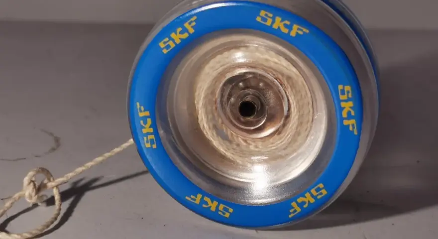 Blå jojo med kullager och texten "SKF" runt kanten. Snöret är knutet och ligger på ett grått underlag.