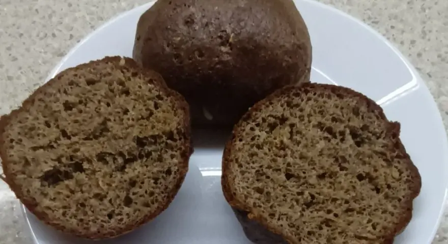 Na talerzu leżą keto bułki babka jajowata. Jedna jest cała, dwie pozostałe przekrojone na pół, ukazując puszyste wnętrze.