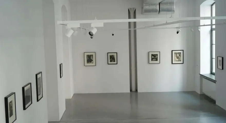 Galeria sztuki z pracami Karola Hillera. Wnętrze z białymi ścianami, szarą podłogą i kilkoma czarno-białymi fotografiami na ścianach.