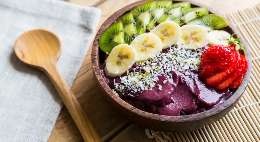 Un bol de smoothie aux fruits d'açaï, garni de bananes, de kiwis, de fraises et de graines.