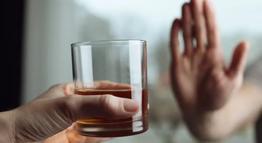 Dłoń odrzuca szklankę z alkoholem, symbolizując koniec z nałogiem i wyciek z wszywki.