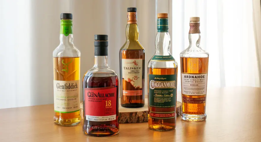 Fünf Flaschen gute Whiskey-Sorten: Glenfiddich, Glenallachie, Talisker, Cragganmore und Ardnahoe stehen auf einem Holztisch.