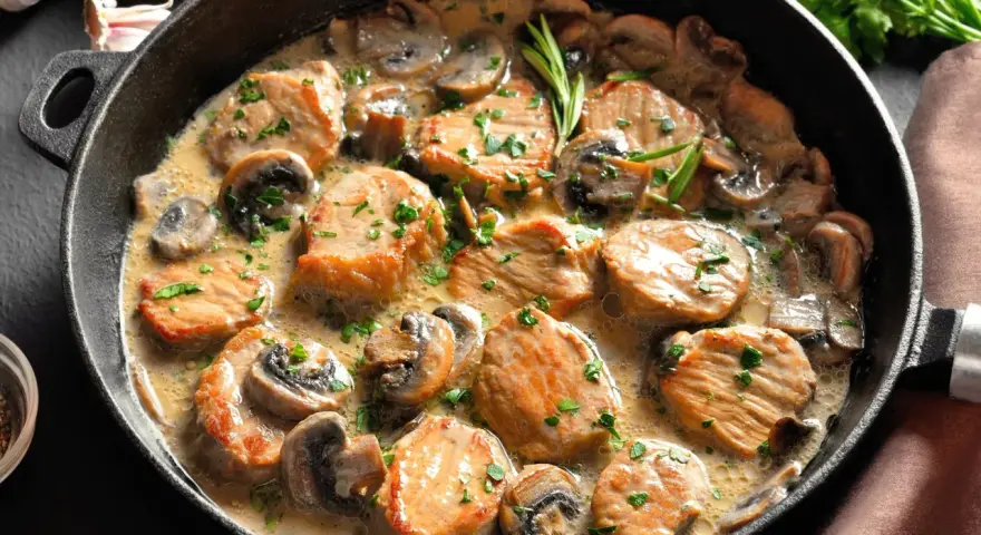 Soczysty schab w sosie pieczarkowym, udekorowany natką pietruszki, podany w żeliwnej patelni. Aromatyczne danie, które zachwyca smakiem.