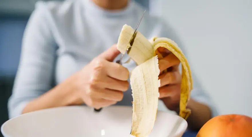 Une personne coupe une banane, riche en potassium, pour prendre soin de son cœur.