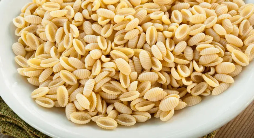 Un primo piatto di gnocchetti sardi, pasta tipica della Sardegna, in un piatto bianco.