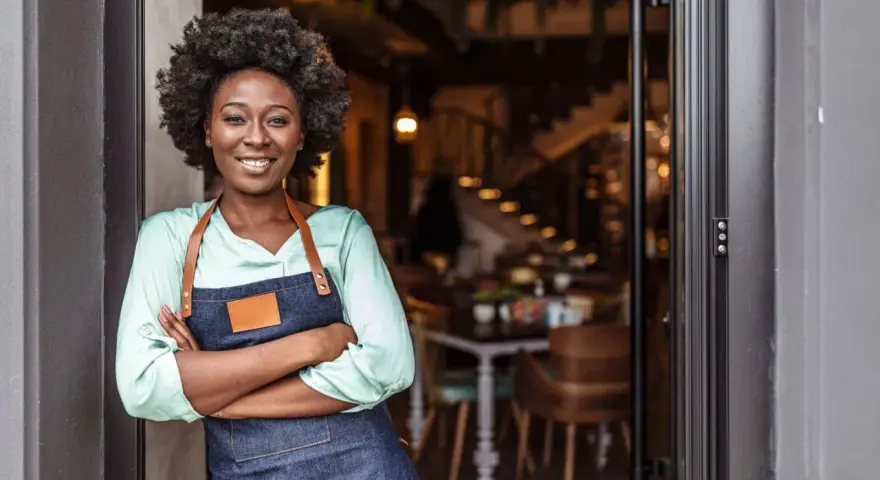 Mujer sonriente con delantal, lista para abrir su restaurante. Su plan de negocio es sólido.