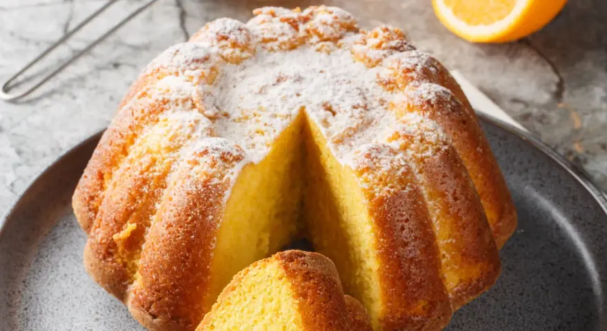 Una fetta di torta all'arancia morbidissima, cosparsa di zucchero a velo, pronta per essere gustata.