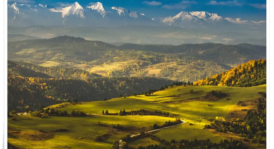 Widok na Tatry z ośnieżonymi szczytami, w tym Trzy Korony. Jesienne wzgórza pokryte złotymi liśćmi i zielonymi łąkami.