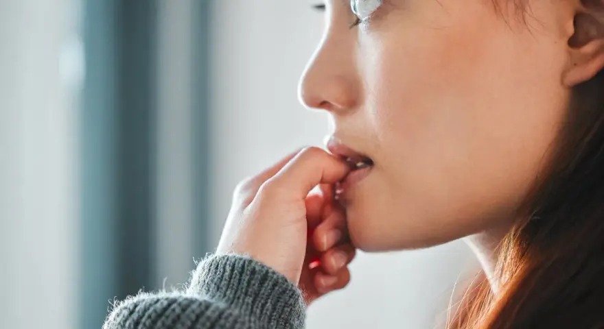 Une jeune femme se ronge les ongles, un signe de stress ou d'anxiété. La signification psychologique de se ronger les ongles est souvent liée à une recherche de réconfort.