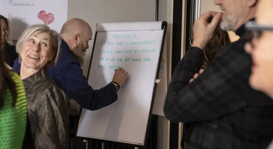 En grupp människor diskuterar hur en bra chef ska vara. En man skriver på en whiteboard om medvetenhet och utveckling.