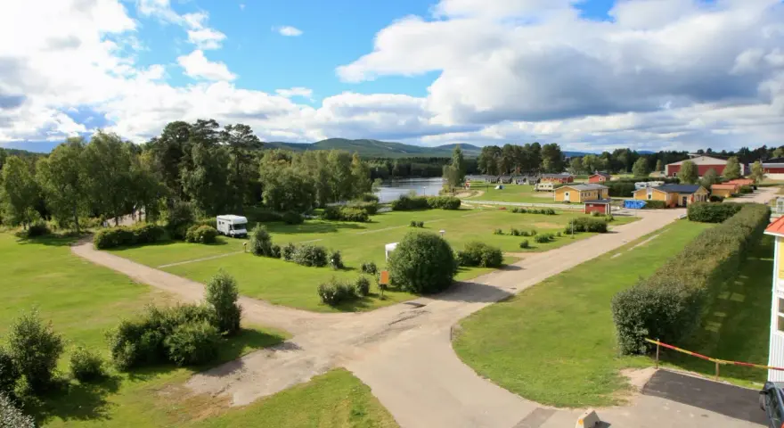 Vacker vy över svegs camping med husbilar, stugor och en sjö i bakgrunden under en molnig himmel.